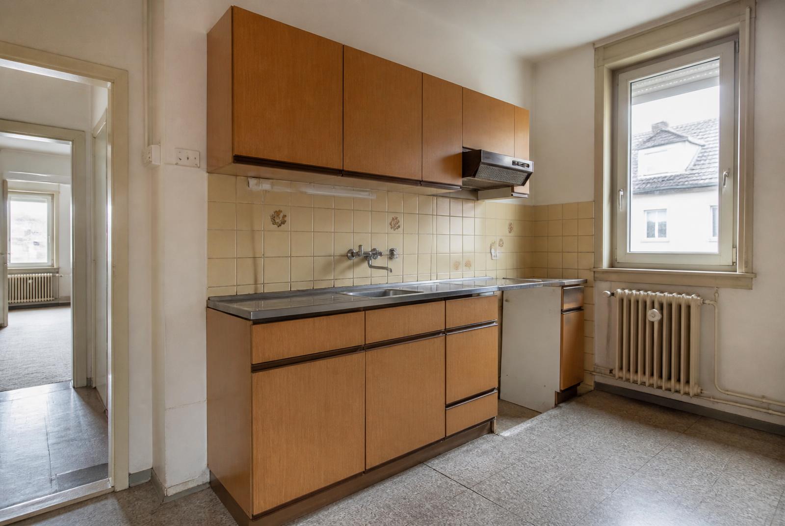 Veraltete Küche mit Holzfronten und vergilbten Fliesen in einem Altbau