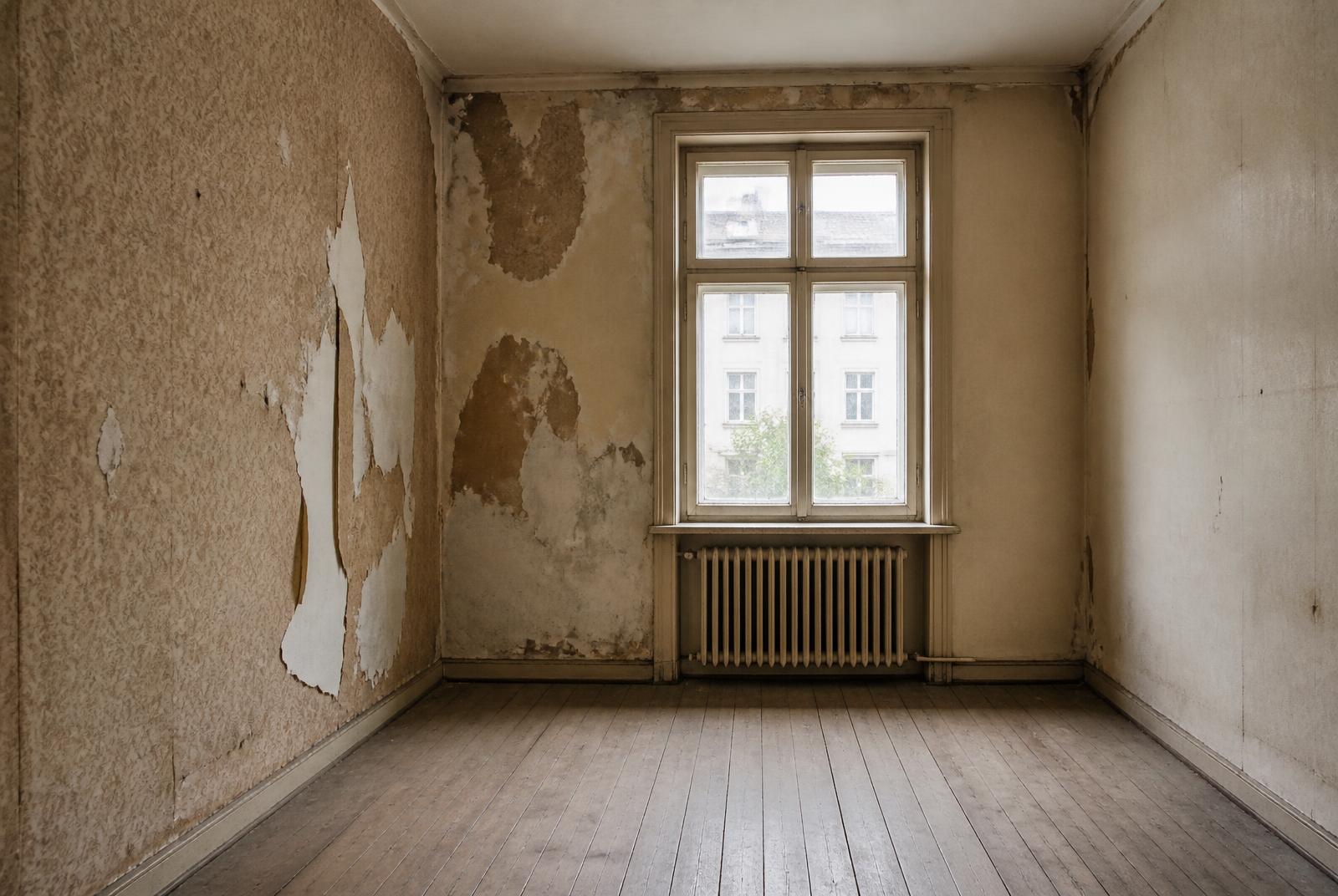 Unsaniertes Schlafzimmer eines Altbaus mit gelösten Tapeten und alten Dielen